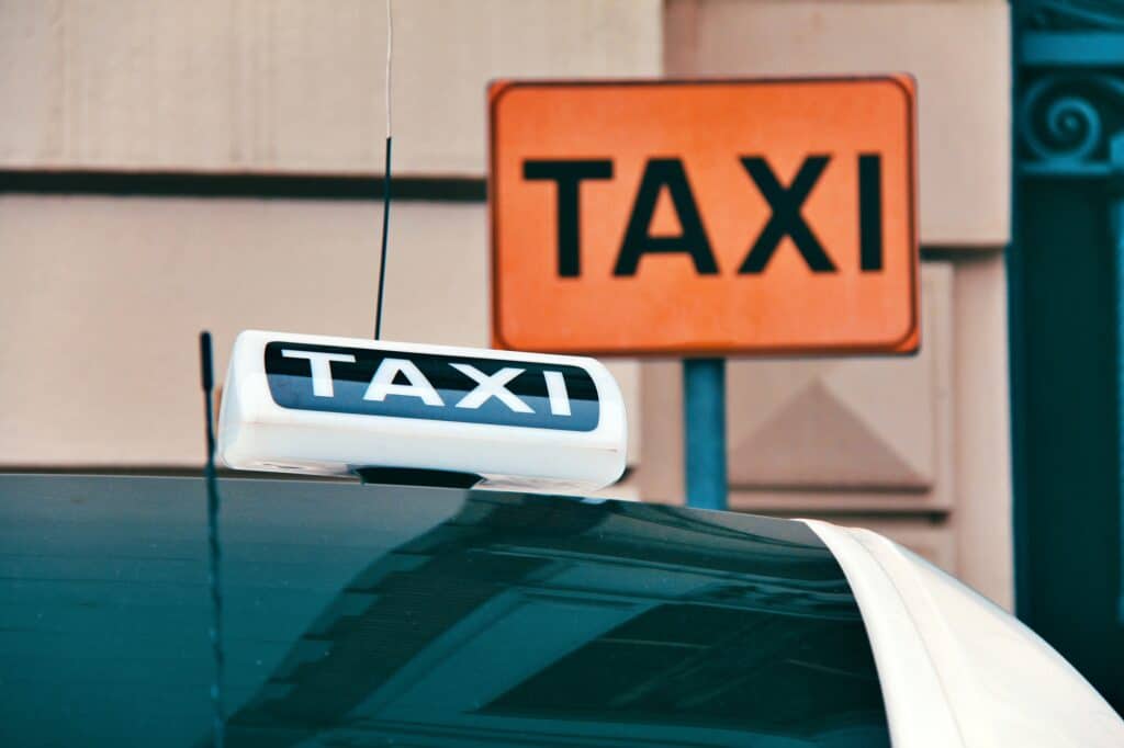 Lumineux de taxi sur le toit d'une voiture garé devant un panneau Taxi.