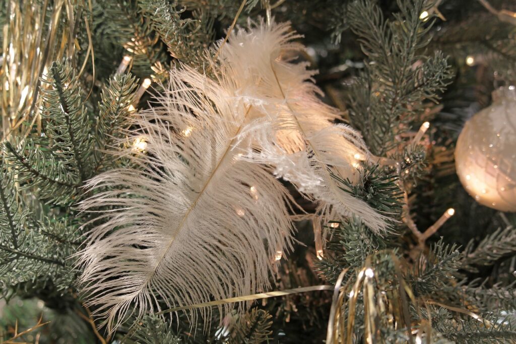 Décoration festive de Noël avec des plumes blanches et des lumières scintillantes sur un sapin, créant une ambiance chaleureuse et élégante.