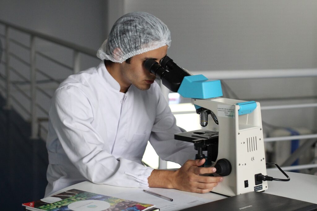 Chercheur en blouse blanche utilisant un microscope dans un laboratoire, symbolisant la recherche scientifique et les innovations technologiques au CEA Cadarache.